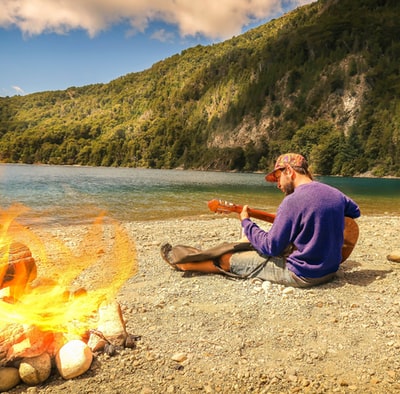 白天，身穿紫色连帽衫的男子坐在靠近水体的灰色沙滩上
